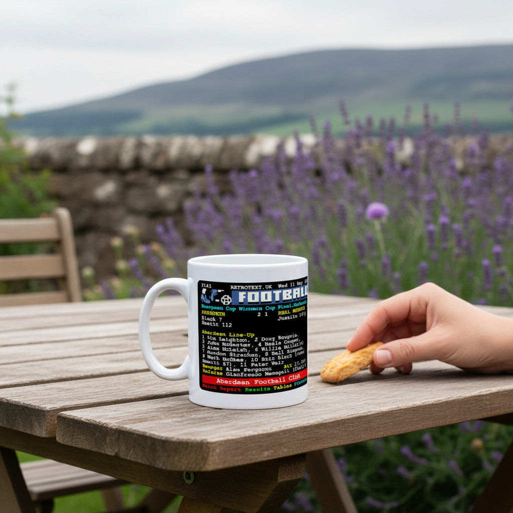 Retrotext Aberdeen 1983 European Cup-Winners' Cup ceramic mug with teletext graphic on a wooden table in a garden.