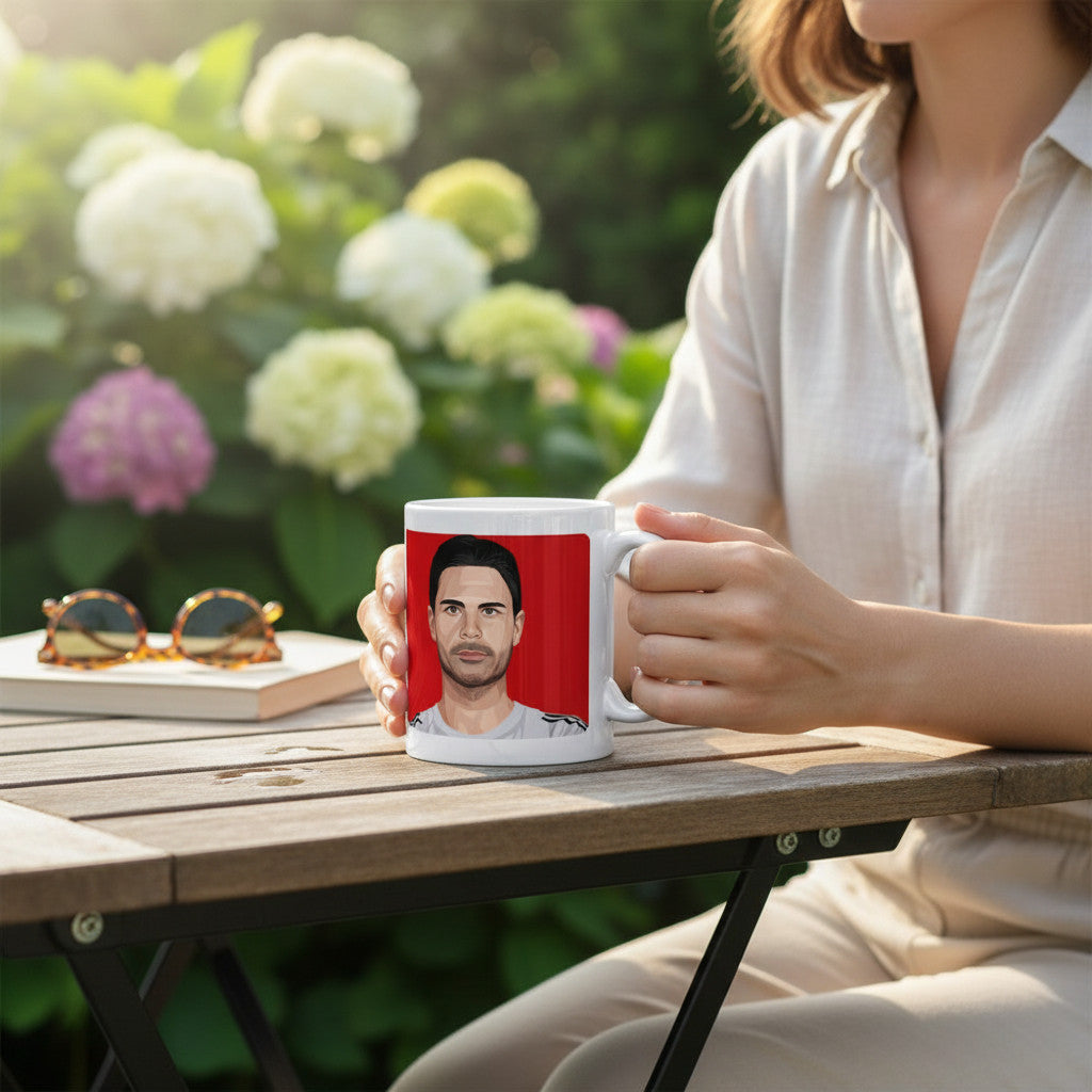 Retrotext Arsenal 2026 Champions mug featuring Mikel Arteta illustration held by a person at an outdoor garden table