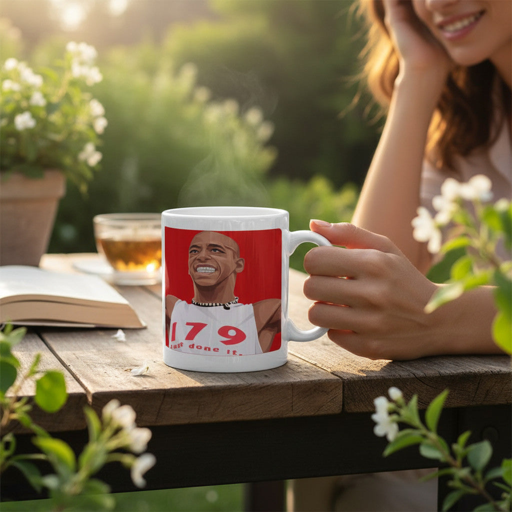 Retrotext Arsenal Ian Wright 179 Just Done It glossy white ceramic mug held by a person at an outdoor garden table.