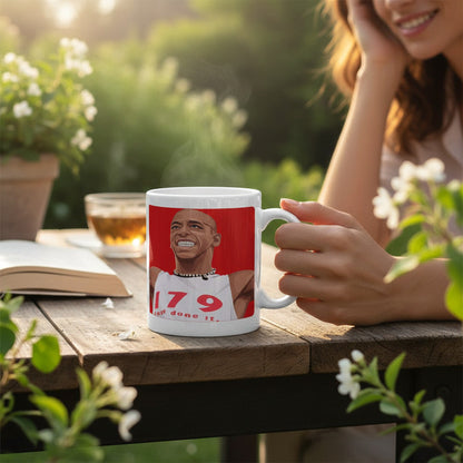 Retrotext Arsenal Ian Wright 179 Just Done It glossy white ceramic mug held by a person at an outdoor garden table.