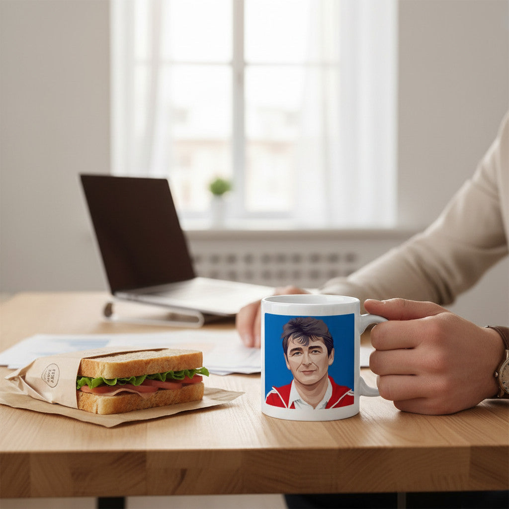 Retrotext white ceramic mug featuring a graphic of Brian Clough, held by a person at a wooden desk with a sandwich.