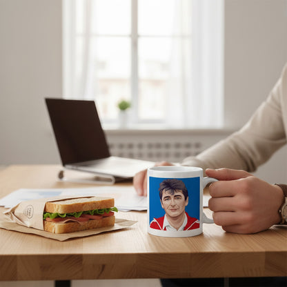 Retrotext white ceramic mug featuring a graphic of Brian Clough, held by a person at a wooden desk with a sandwich.
