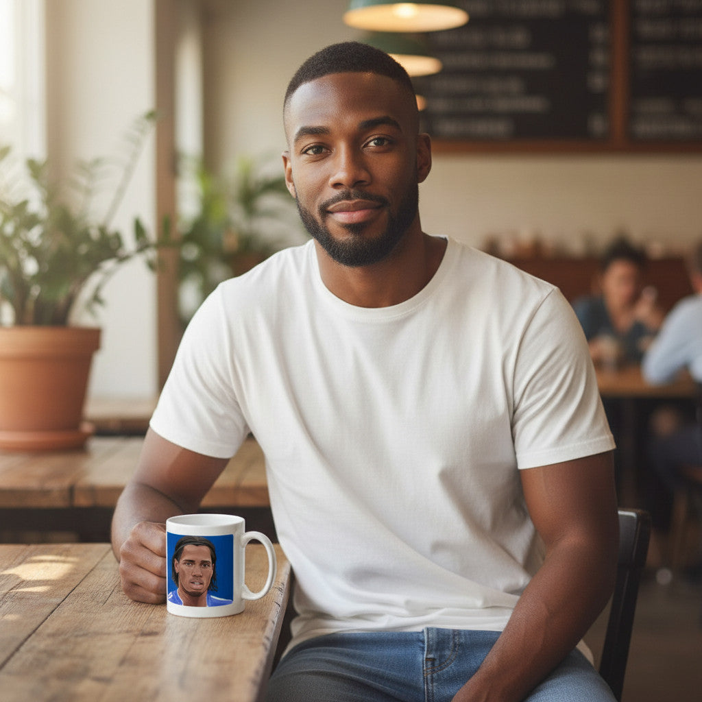 Retrotext white ceramic mug featuring Didier Drogba, held by a man sitting at a wooden cafe table.