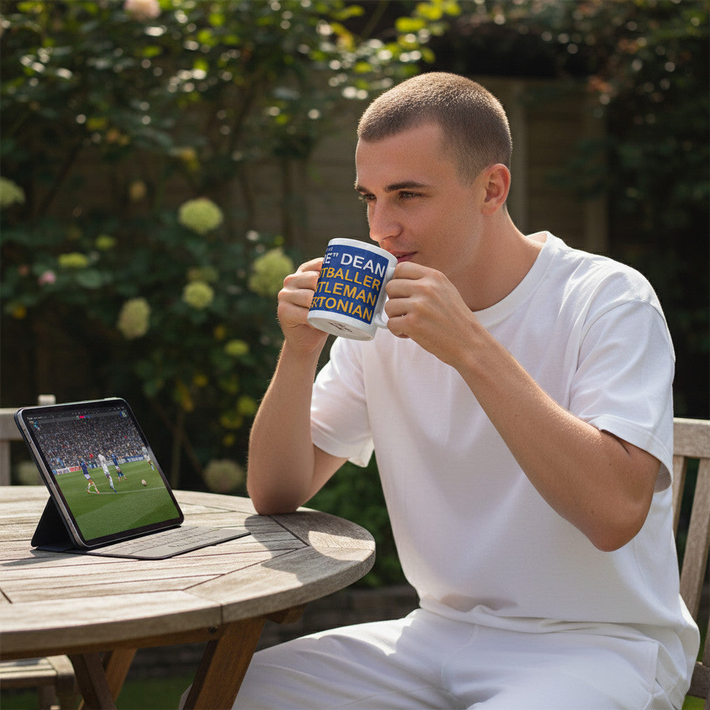 Retrotext Dixie Dean Everton football mug held by a man watching a match on a tablet in a garden setting.