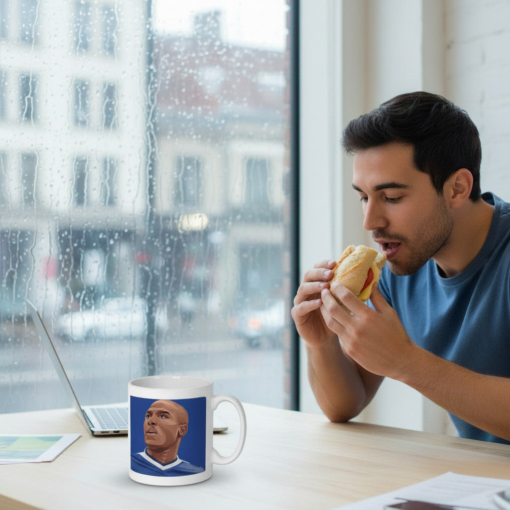 Retrotext white ceramic mug featuring Kevin Campbell 1999 goal illustration on a desk next to a man eating a sandwich