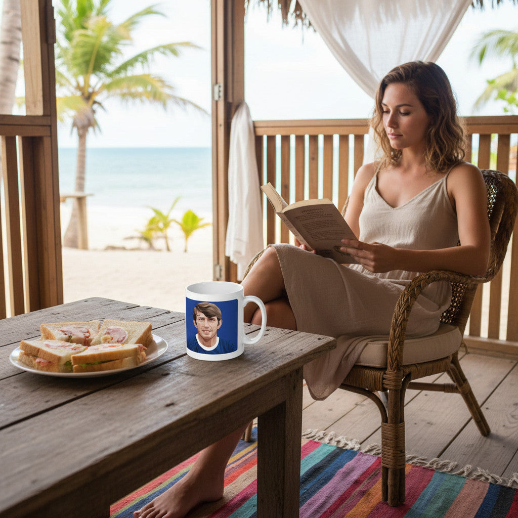 Retrotext 11oz glossy white mug featuring Howard Kendall, placed on a wooden table next to sandwiches by the beach.