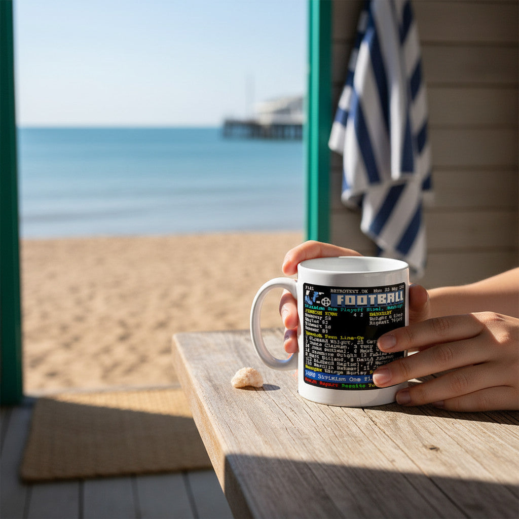 Retrotext white ceramic mug featuring Ipswich Town 2000 playoff final stats held by hands on a beachside wooden table.