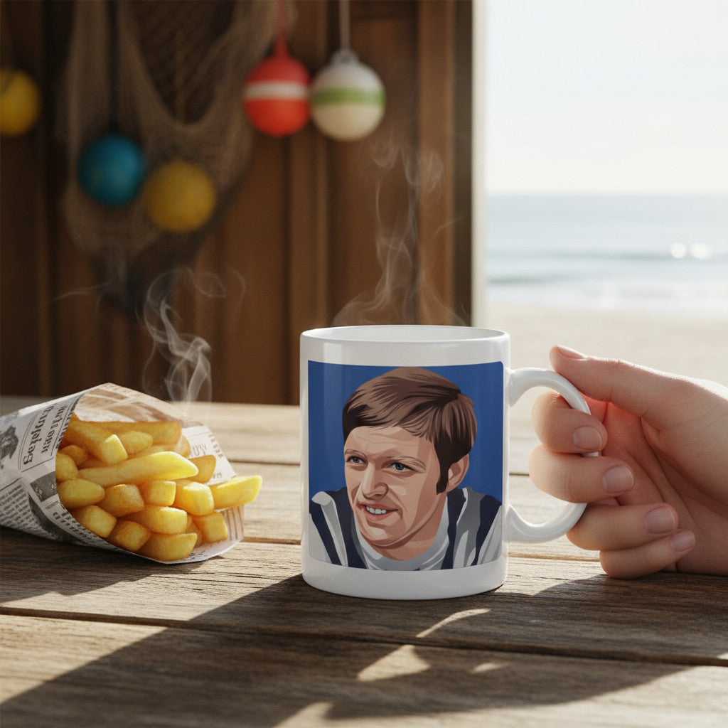Retrotext white ceramic mug featuring an illustration of Jeff Astle, held on a wooden table with chips by the beach.