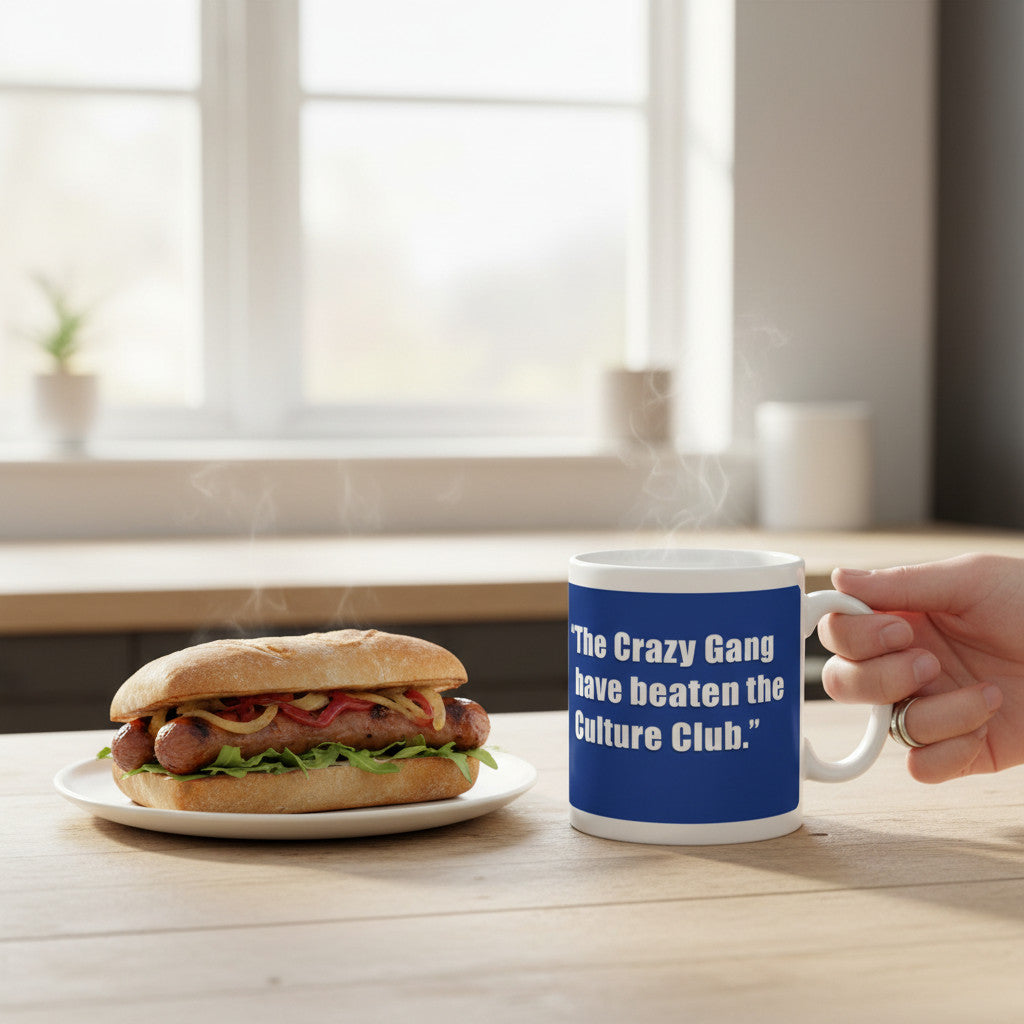 Retrotext white 11oz mug featuring the John Motson Crazy Gang quote next to a hot sausage sandwich on a wooden table.