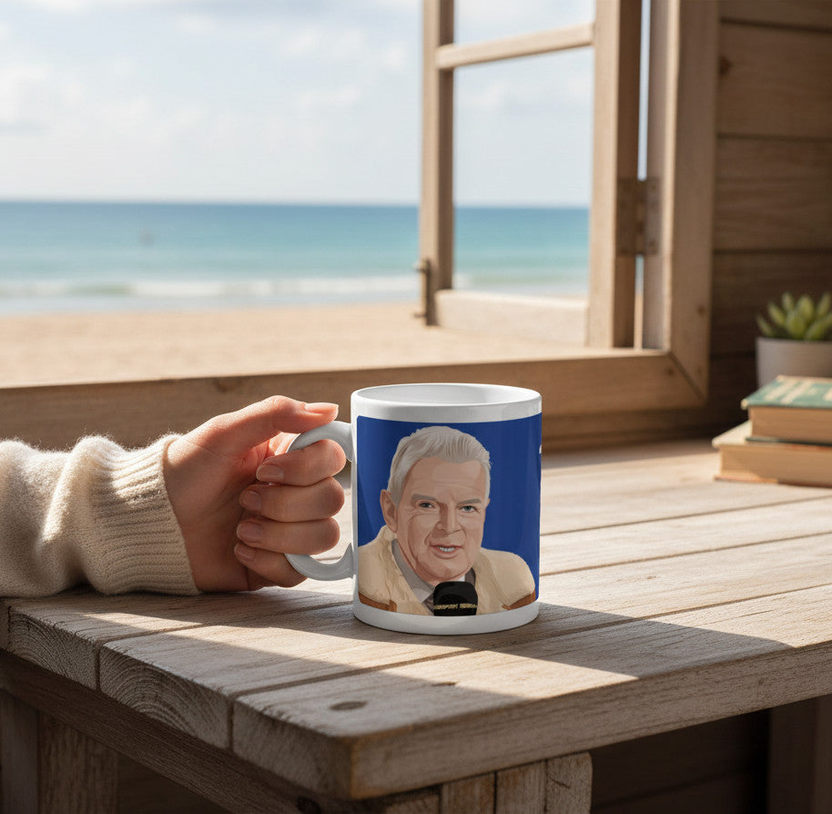 Retrotext white ceramic mug featuring a John Motson illustration, held on a wooden table by a beach window.