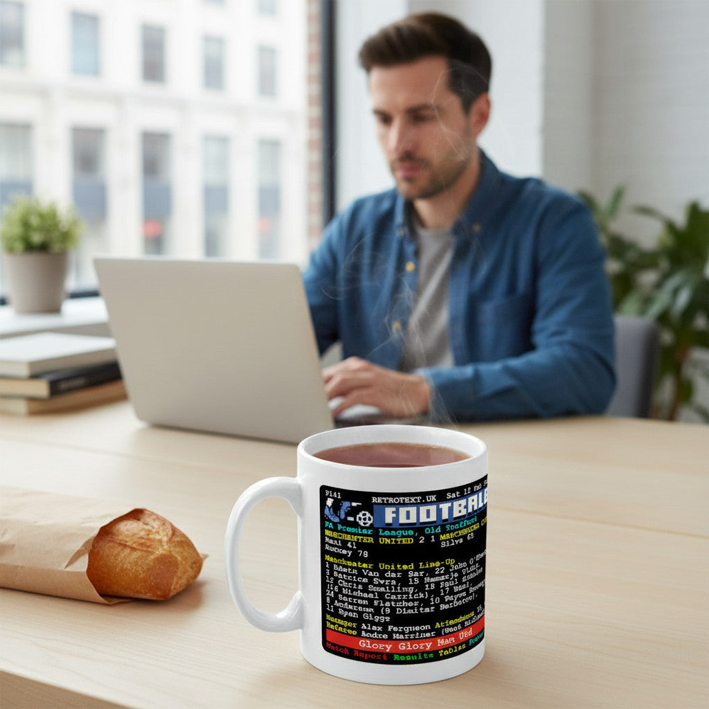 Retrotext ceramic mug featuring a 2011 Manchester United vs Manchester City teletext match report on a desk