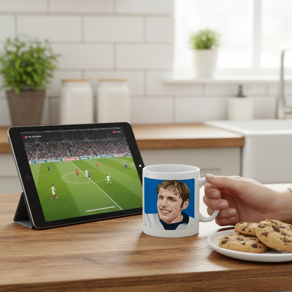 Retrotext 11oz glossy white mug featuring a Ronnie Radford illustration, held on a desk next to a tablet and cookies.